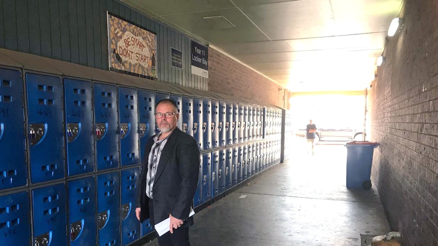A man standing in a corridor beside school lockers.