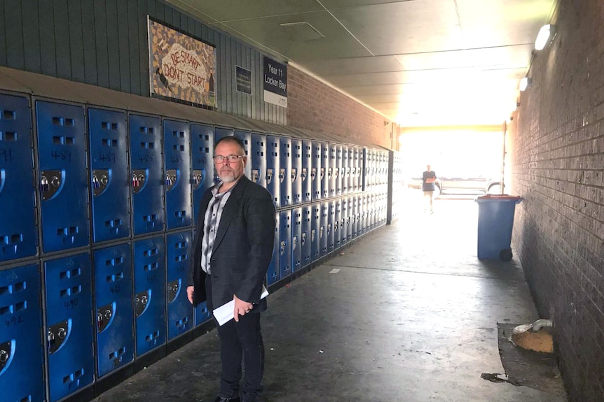 A man standing in a corridor beside school lockers.
