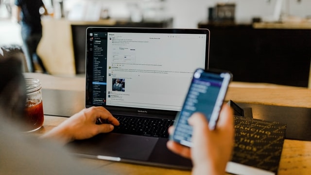 A person working on a laptop with their Slack channel open and mobile out.