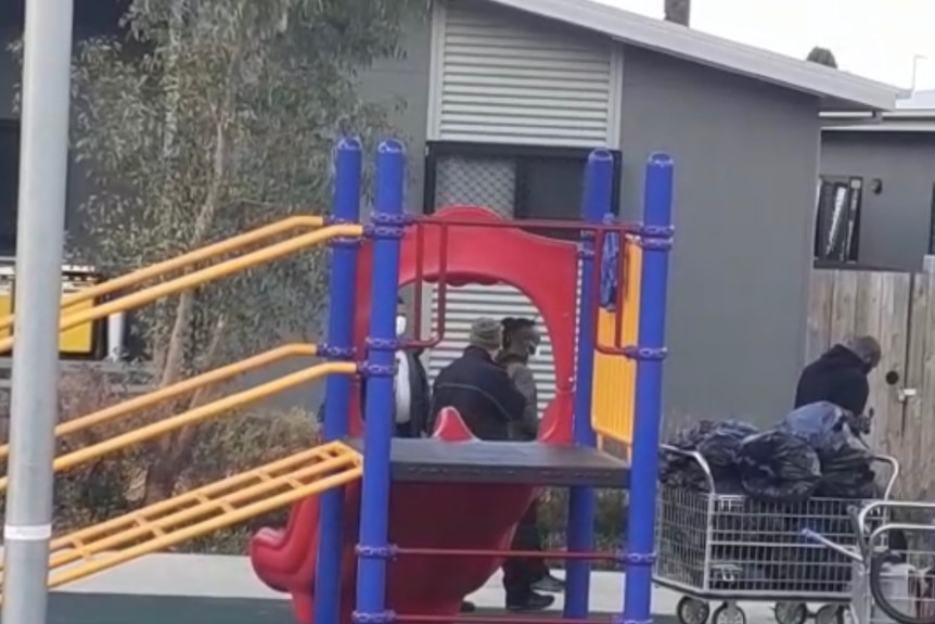 Four people stand around an outdoor playground in close contact with each other.