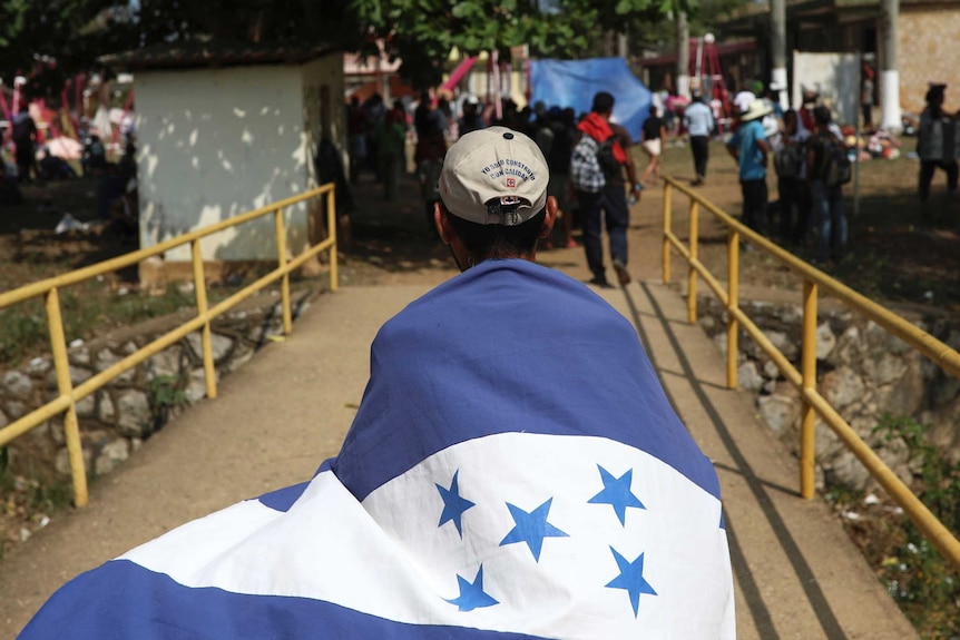 A migrant wrapped in the Honduras flag walks across a small bridge