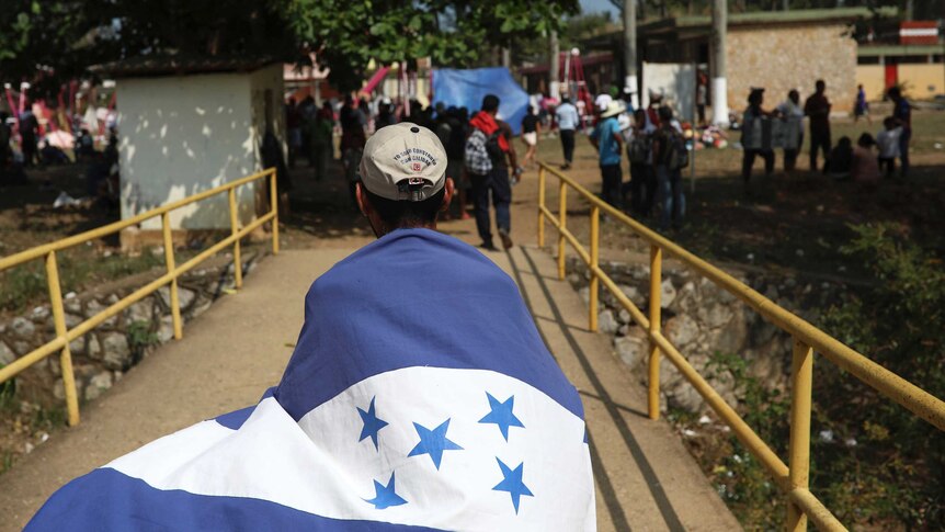 A migrant wrapped in the Honduras flag walks across a small bridge