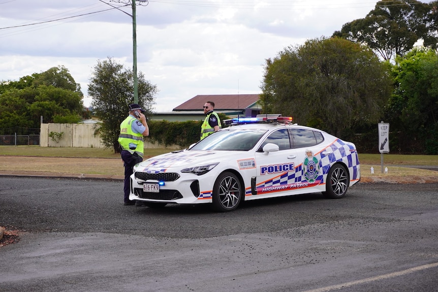 Officers stand near a parked police car on River Road, Kingaroy