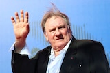 A man in a suit with his hand up and waving.
