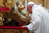 Pope Francis kisses a statue of baby Jesus as he leads the Christmas night Mass in Saint Peter's Basilica