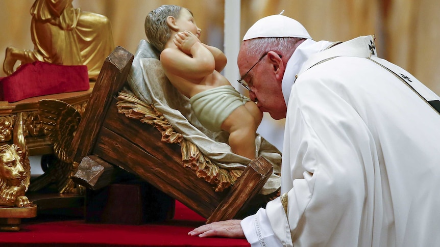Pope Francis kisses a statue of baby Jesus as he leads the Christmas night Mass in Saint Peter's Basilica