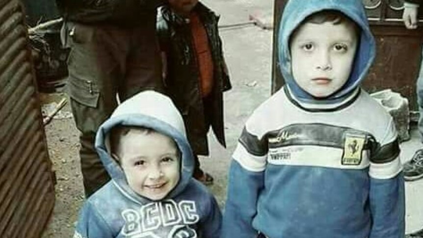Two children look at the camera while holding hands in besieged Eastern Ghouta.