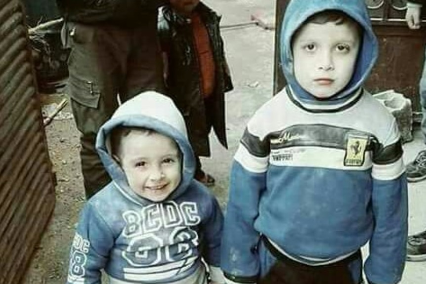 Two children look at the camera while holding hands in besieged Eastern Ghouta.