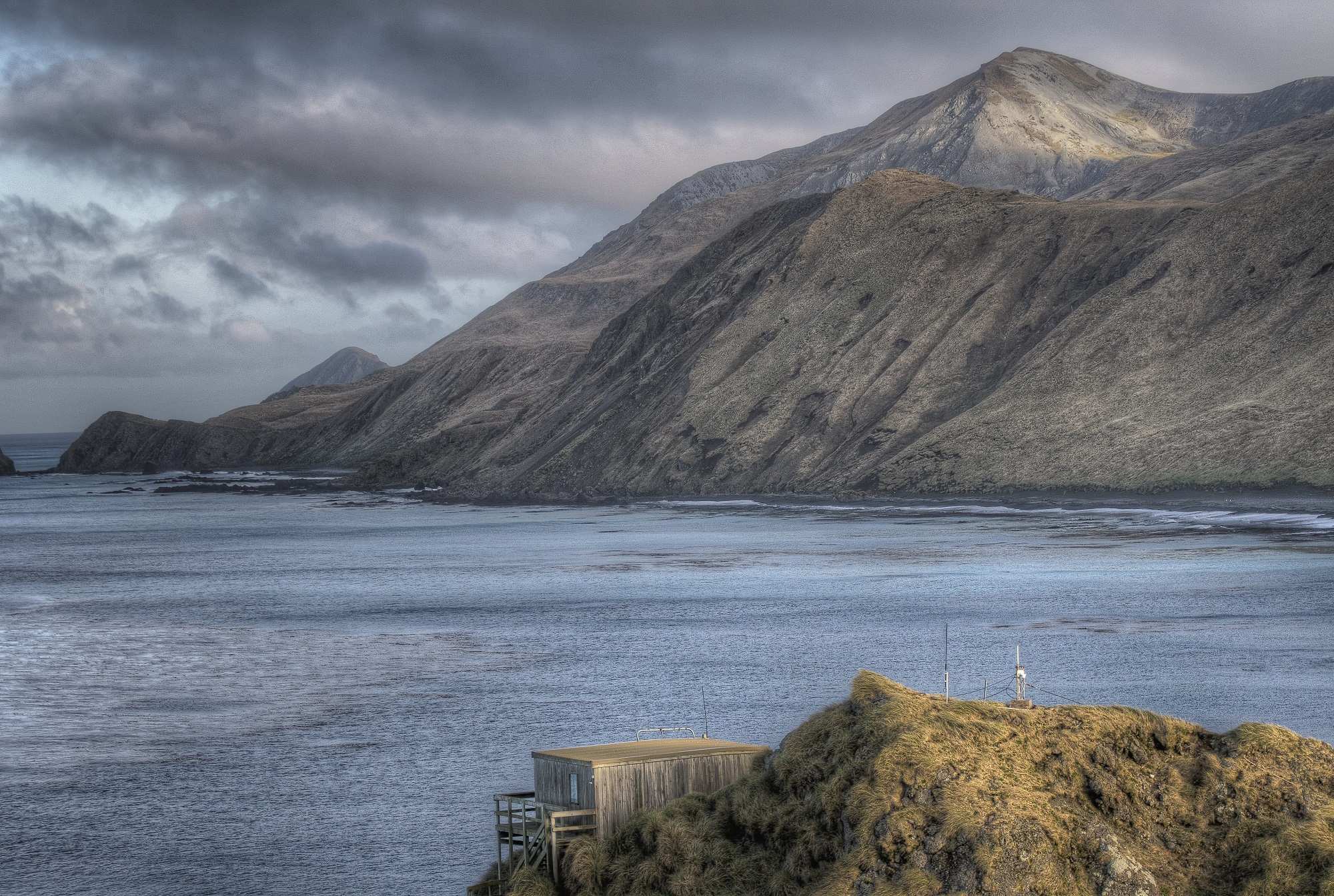 A small wooden shack blends into the rugged mountainous coastline of Macquarie Island