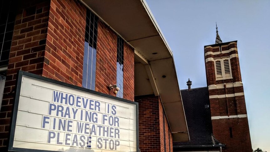 A message on a church noticeboard saying 'whoever is praying for fine weather please stop'.