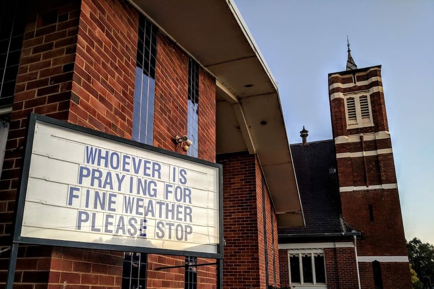 A message on a church noticeboard saying 'whoever is praying for fine weather please stop'.