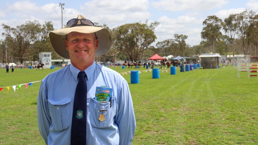 A man in a blue shirt and a broad-brimmed hat stands in the field at an agricultural show