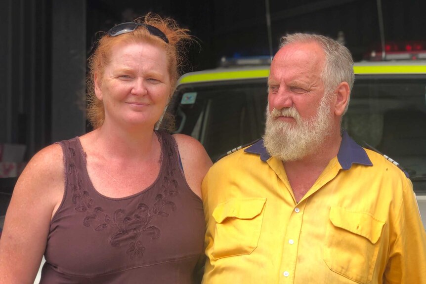 A woman and a man lean on a fire truck. The woman looks at the camera, the man wears a RFS uniform