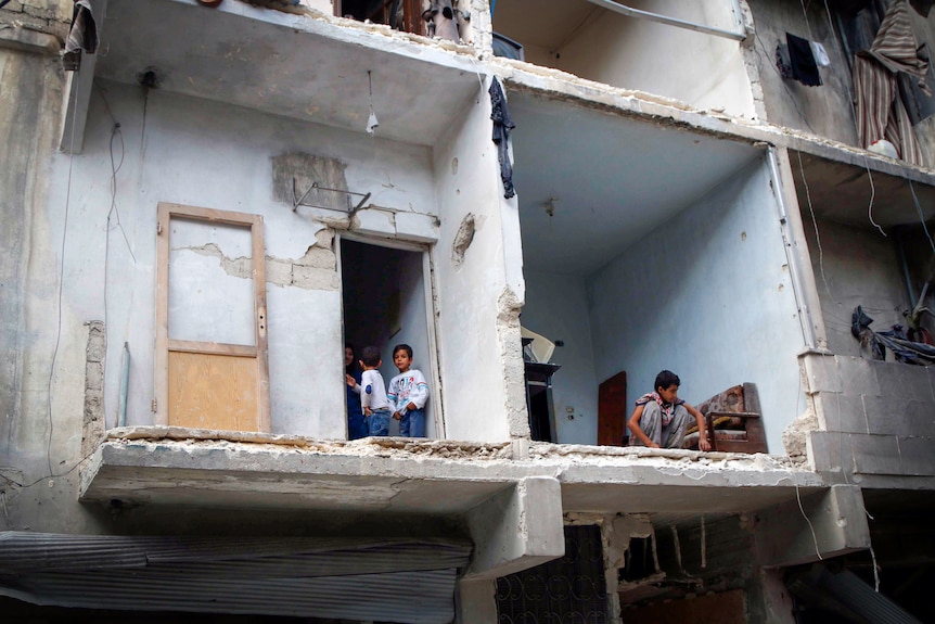 Little boys stand in an apartment, where the wall has been blown out by a missile strike