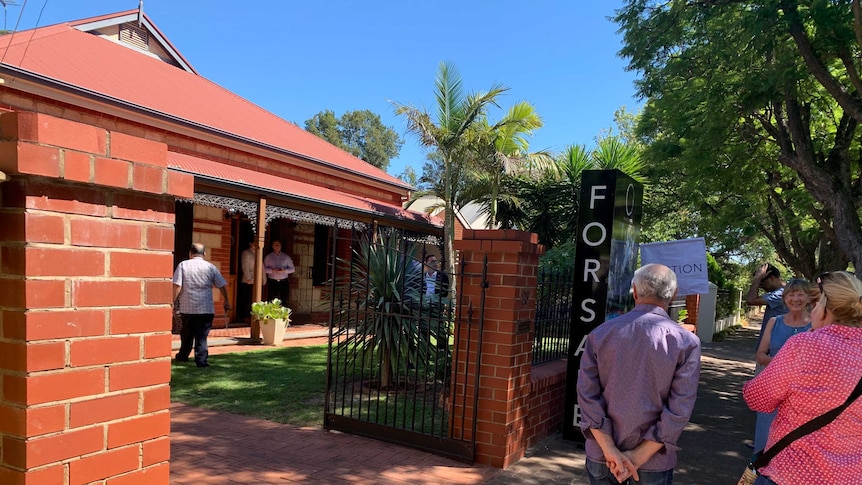 People stand outside the gates of a house for auction at Clarence Park.A large 'FOR SALE' sign is erected nearby.