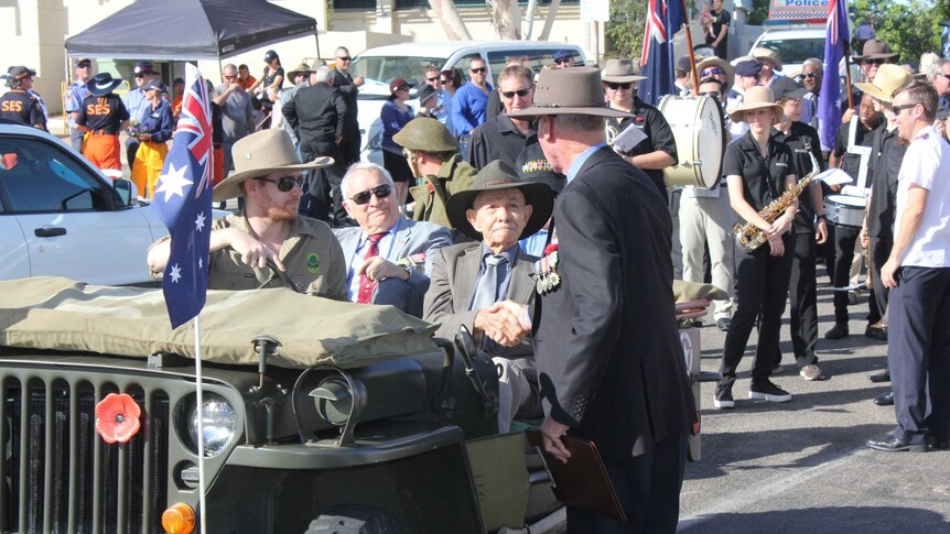 Bill Fortune sits in the front of an army jeep, dressed in a suit and tie