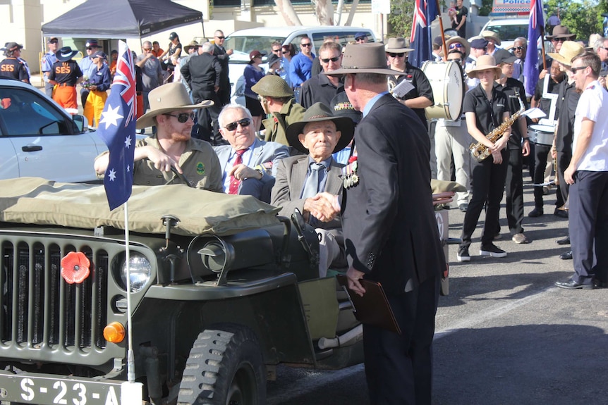 Bill Fortune sits in the front of an army jeep, dressed in a suit and tie