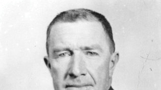 A black and white portrait of a man wearing a tie and suit.