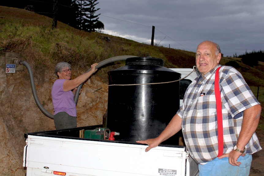 A man and a woman stand next to a ute while as they fill a water tank with a hose connected to a natural spring