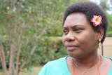 A woman with a flower in her hair stares off into the distance.