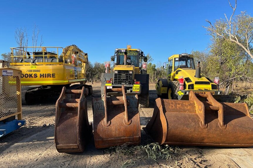 Heavy earthmoving equipment lined up in scrubland.