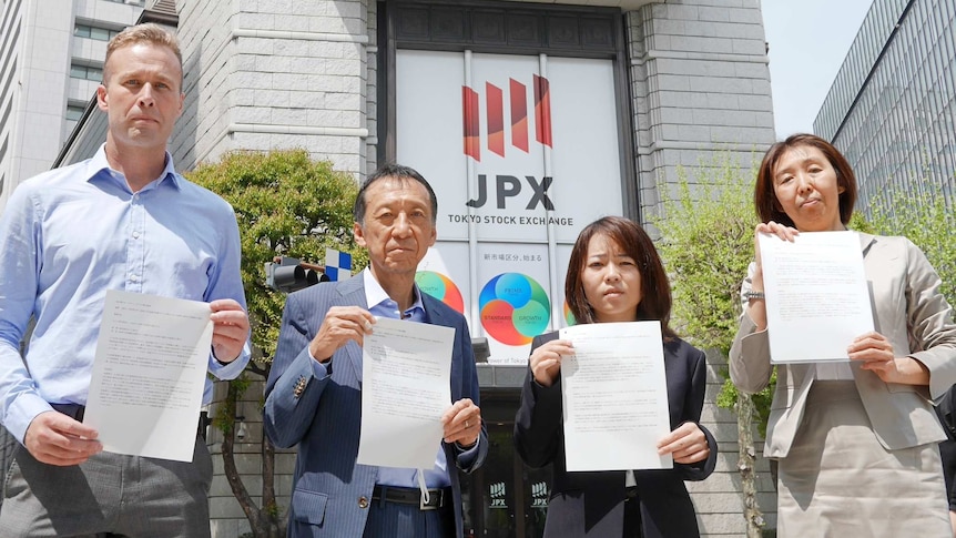 One Anglo-Australian man and three Japanese people hold shareholder demand letters in front of the Japanese stock exchange