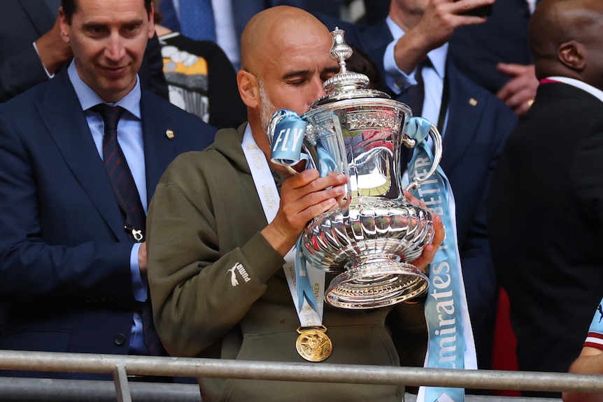 A male football manager kisses the FA Cup following Manchester City's victory in the final.