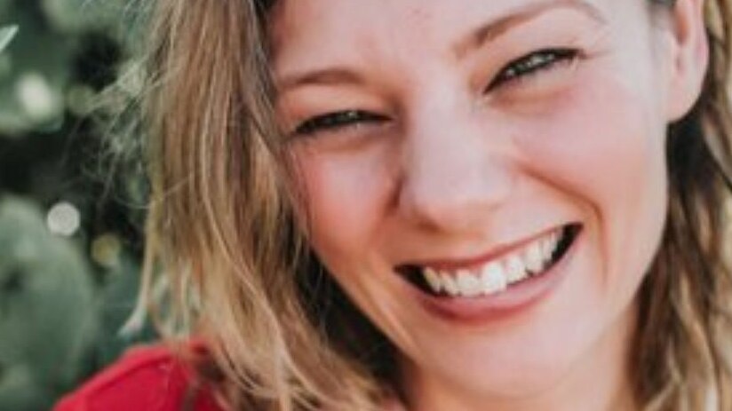 A close-up headshot of Angela Cuming, who is smiling and has her hand resting on her shoulder.