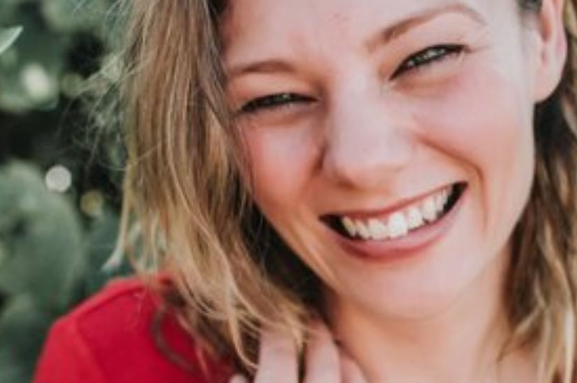 A close-up headshot of Angela Cuming, who is smiling and has her hand resting on her shoulder.