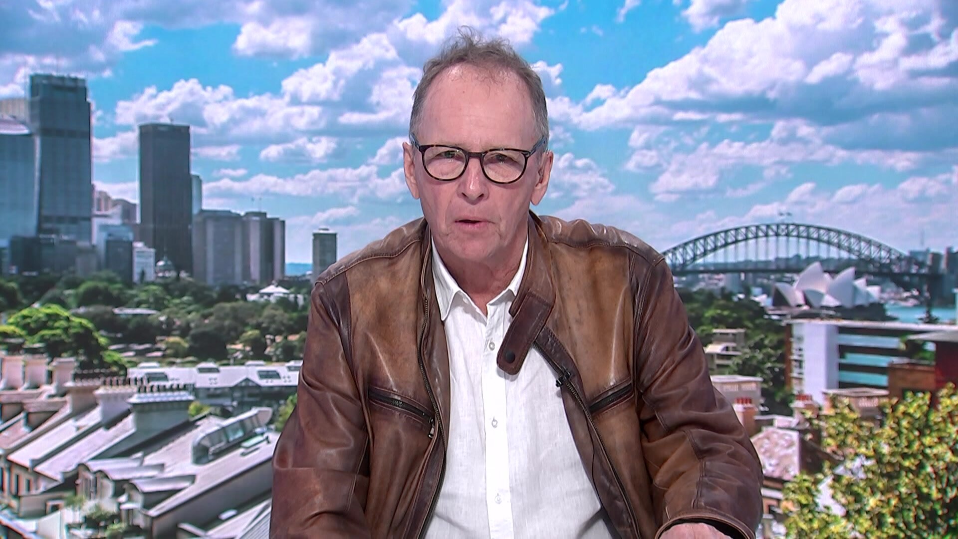 Guy in leather jacket interviewed in front of harbour bridge background. 