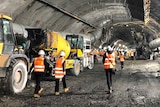 Workers pictured walking away from the camera next to machinery in a huge underground tunnel.
