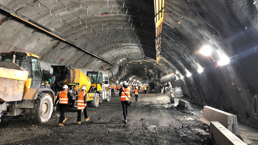 Workers pictured walking away from the camera next to machinery in a huge underground tunnel.