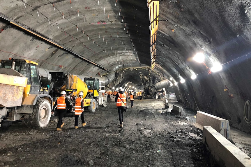 Workers pictured walking away from the camera next to machinery in a huge underground tunnel.