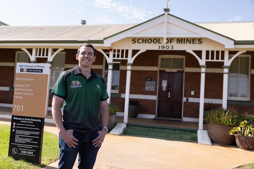 A man who works as a professor standing in front of an old building with School of Mines written on the entrance.  