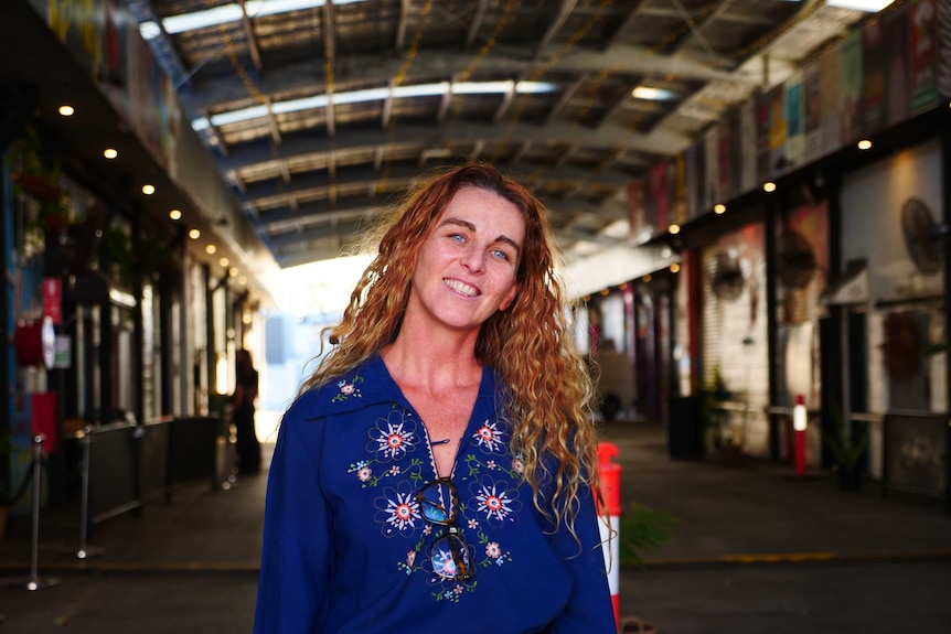 A woman smiles while standing in the driveway of a covered market venue.