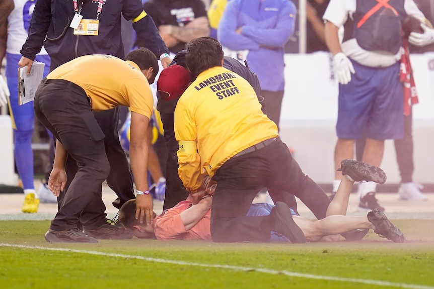 Security guards hold a pitch invader's hands behind his back as they keep him on the ground after chasing him down.