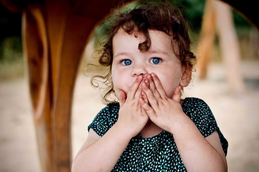 A toddle with her hands over her mouth