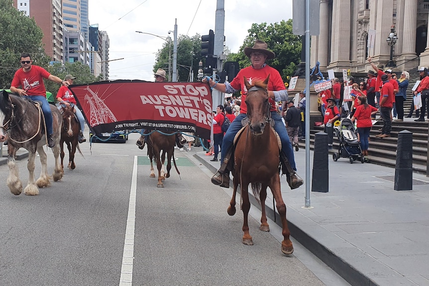 People holding banners ride horses down a city street.