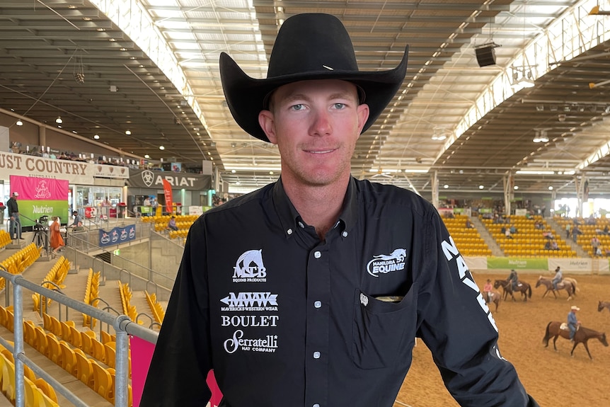 A man in a black hat and shirt stands in front of a sales ring.