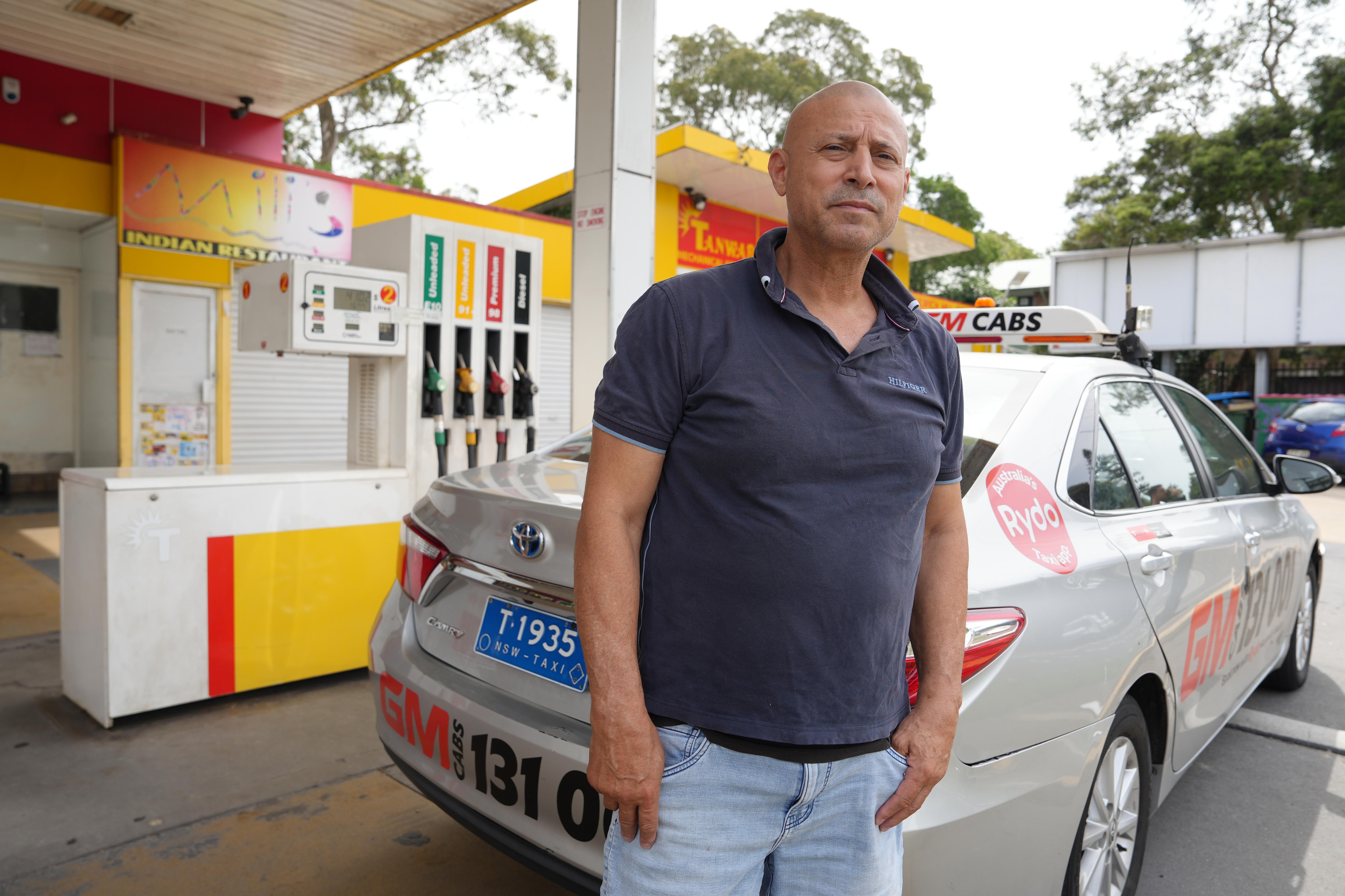 Frank stands behind a taxi parked at a service station, looking concerned.