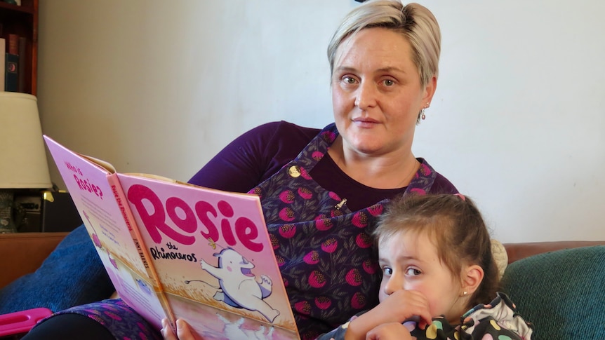 A woman and a young girl sitting on a couch with a book