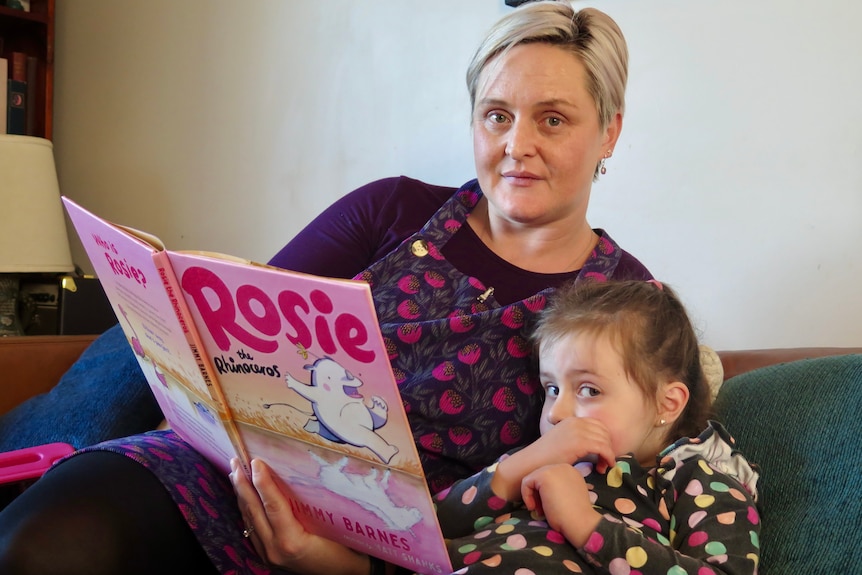 A woman and a young girl sitting on a couch with a book