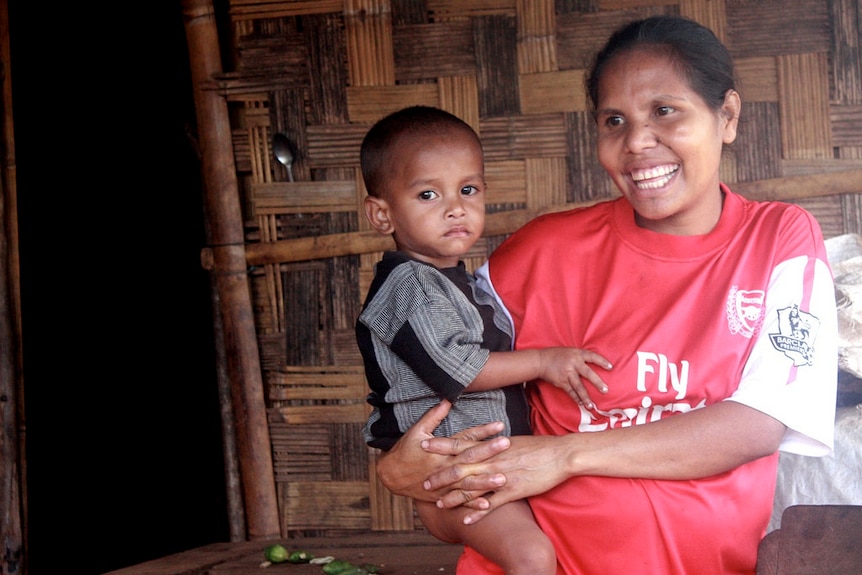 A woman holds her son with a big smile on her face in Timor Leste.