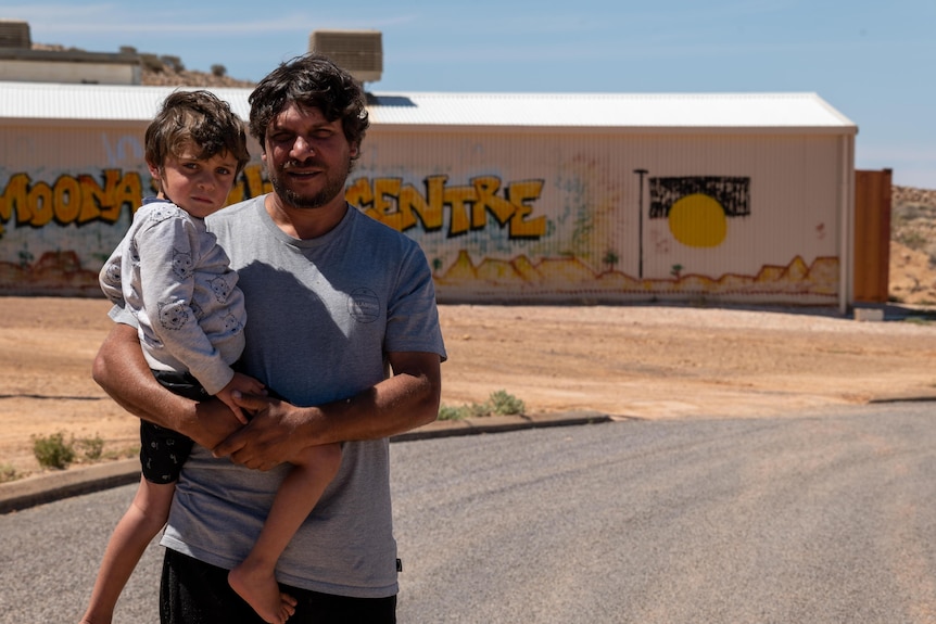 A man holding a young child with a shed in the background