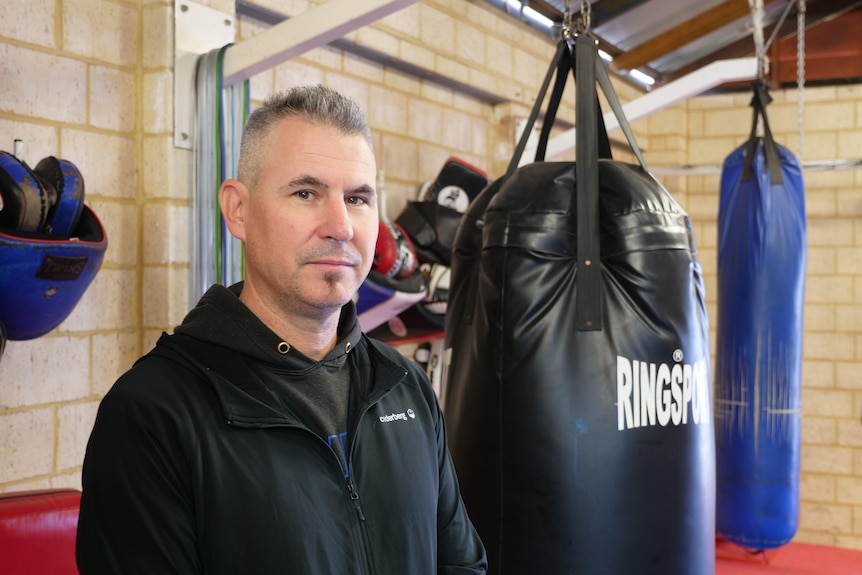 A man stands inside a gym with boxing bags hanging from the ceiling.