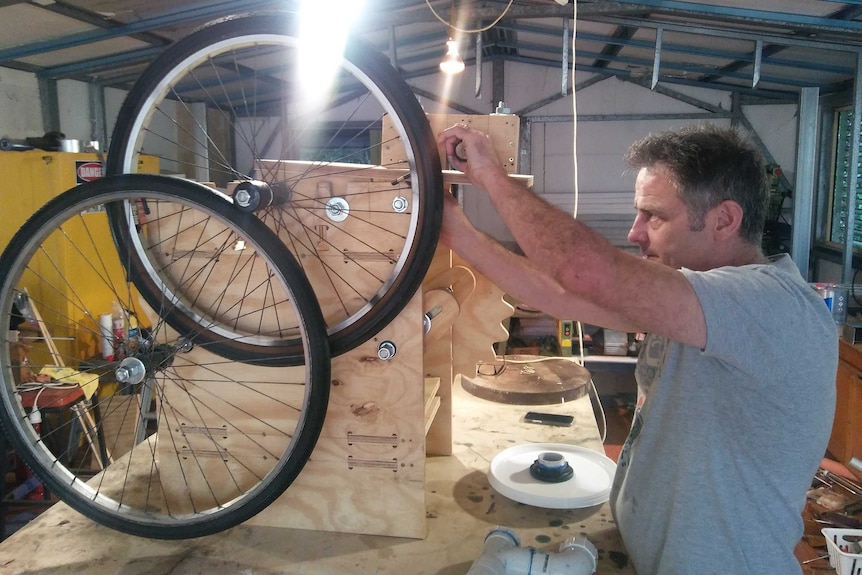 A man uses a screw driver to adjust a hand build machine.