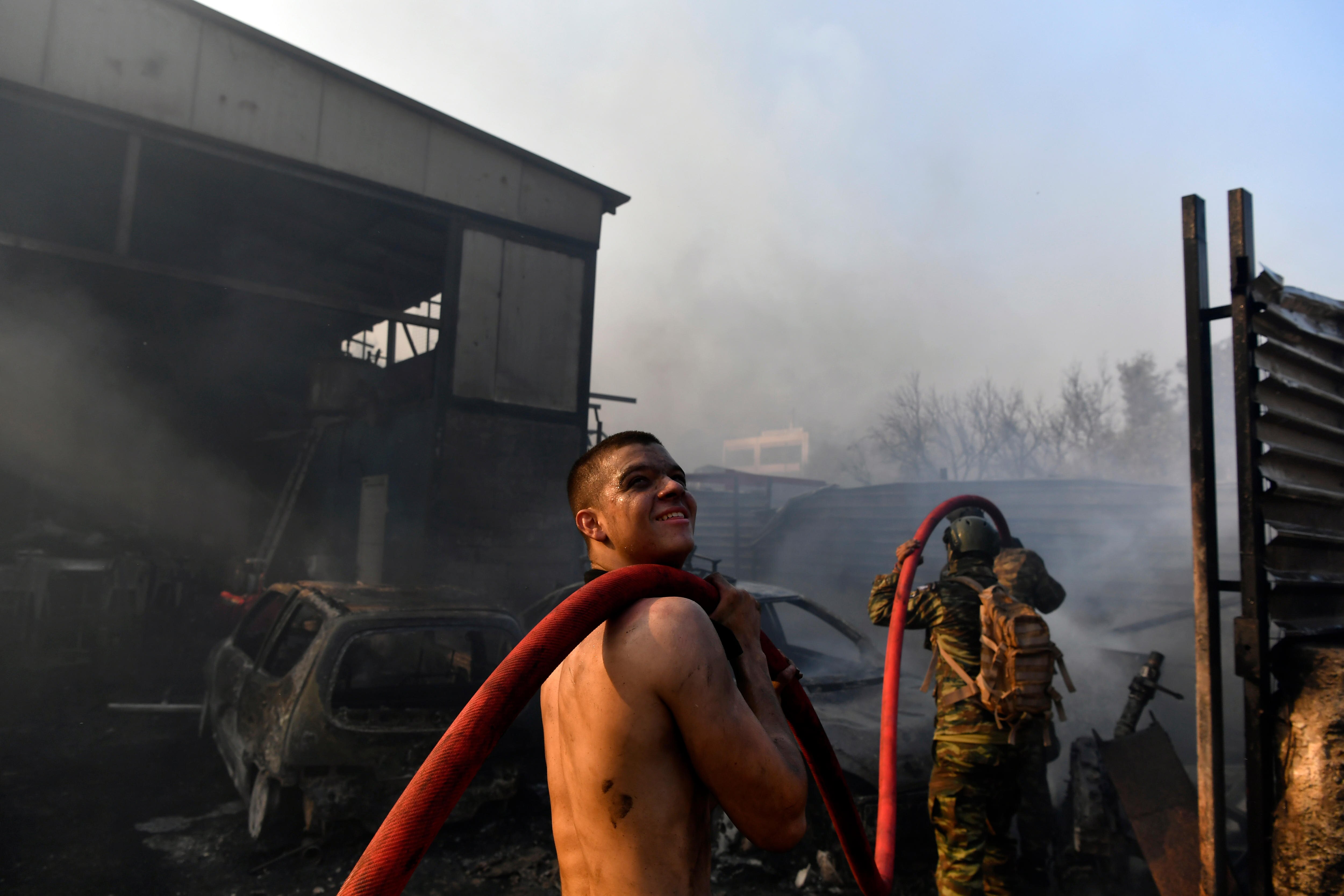 Two men carry a firehose into a burned-out building.
