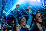 Adults on stage in blue costumes and stage lights with hands in air