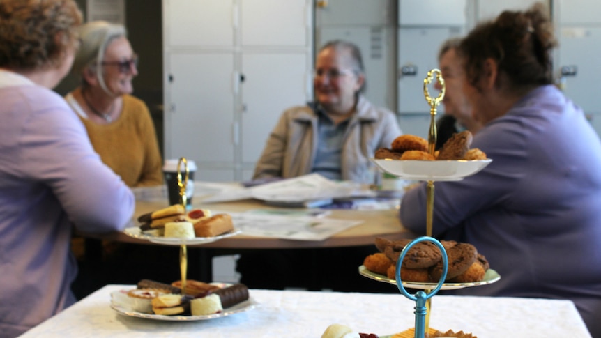 Two stands of cakes in front of a table of older women talking