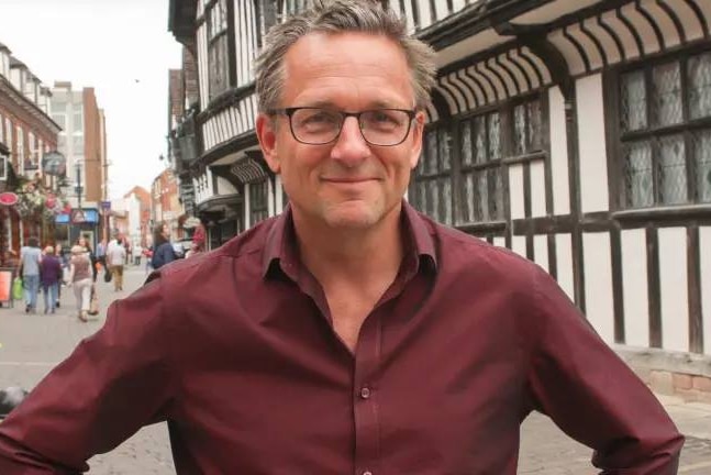 Michael Mosley stands in front of a building in a street.